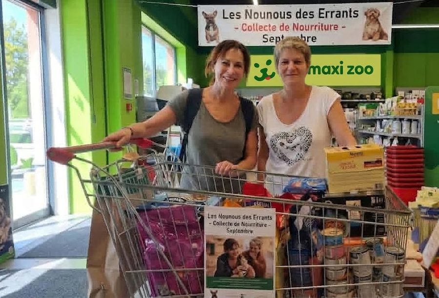 Deux bénévoles des Nounous des Errants derrière un caddie rempli de nourriture pour animaux, sous une banderole de la collecte